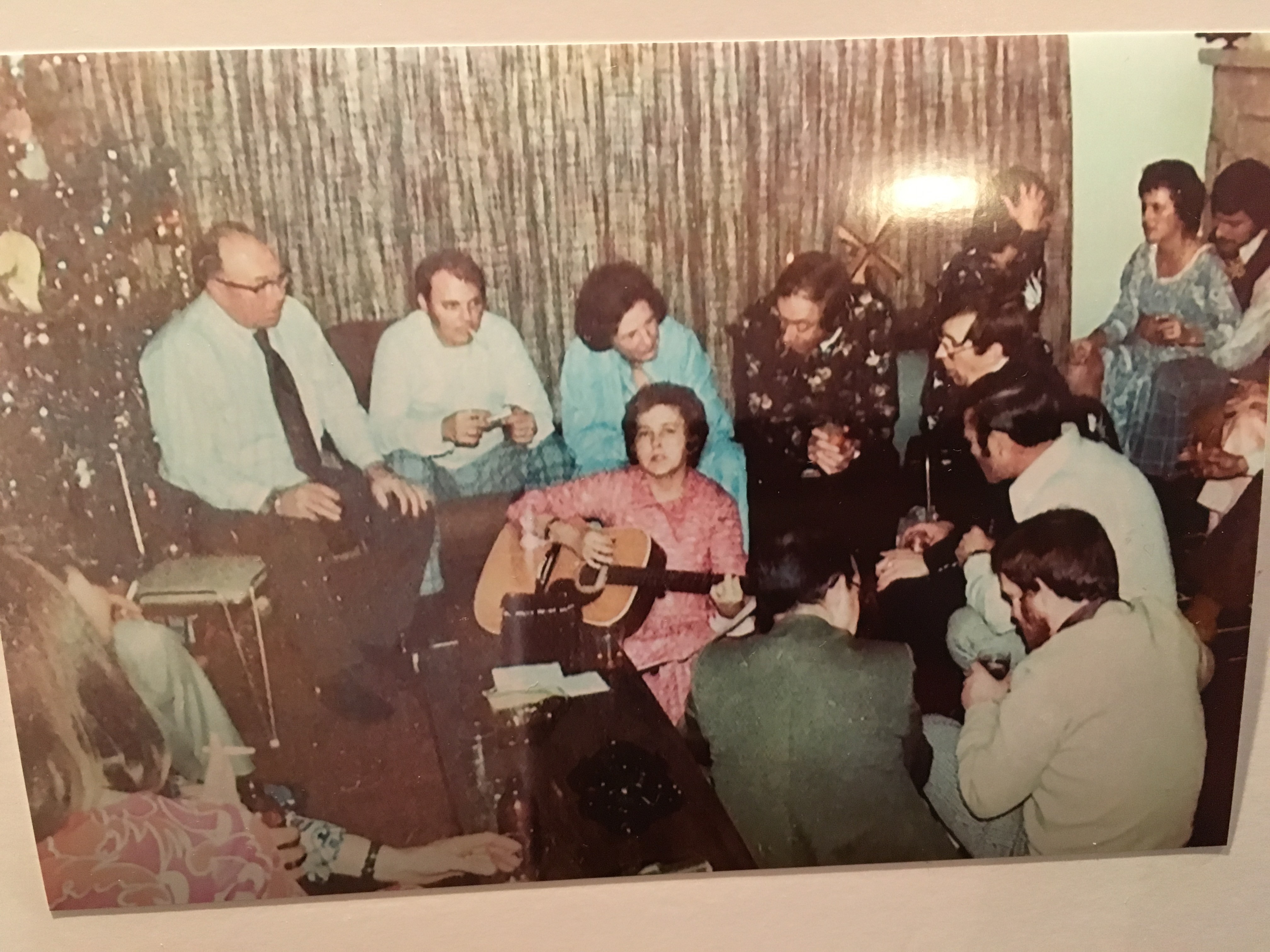 Woman surrounded by a group of people watching her play the guitar. 