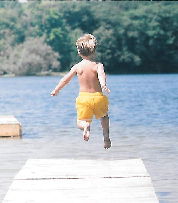 Boy jumping off dock into a lake. 