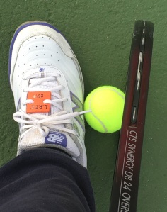 Woman picking up tennis ball using a shoe and the racquet
