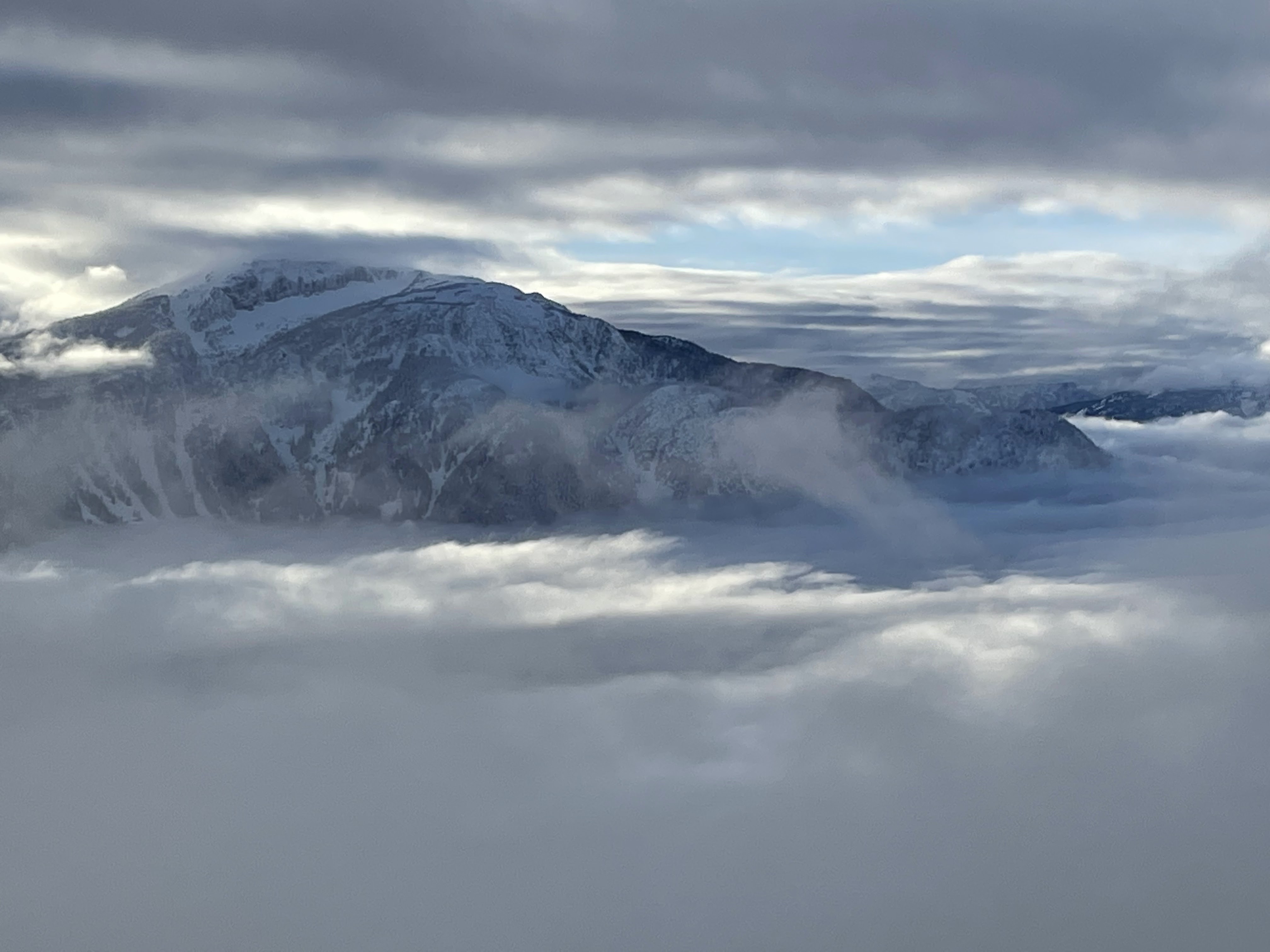 View from the peak of Revelstoke Ski Resort. The sun breaking through clouds and illuminating a distant mountain peak. 